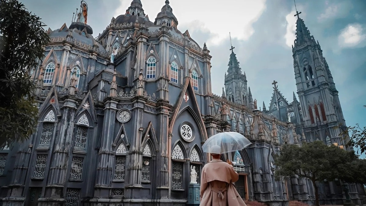 Nhà thờ kiến trúc Gothic nhiều tháp nhọn, một du khách mặc áo khoác cầm ô trong suốt đứng ngắm phía trước