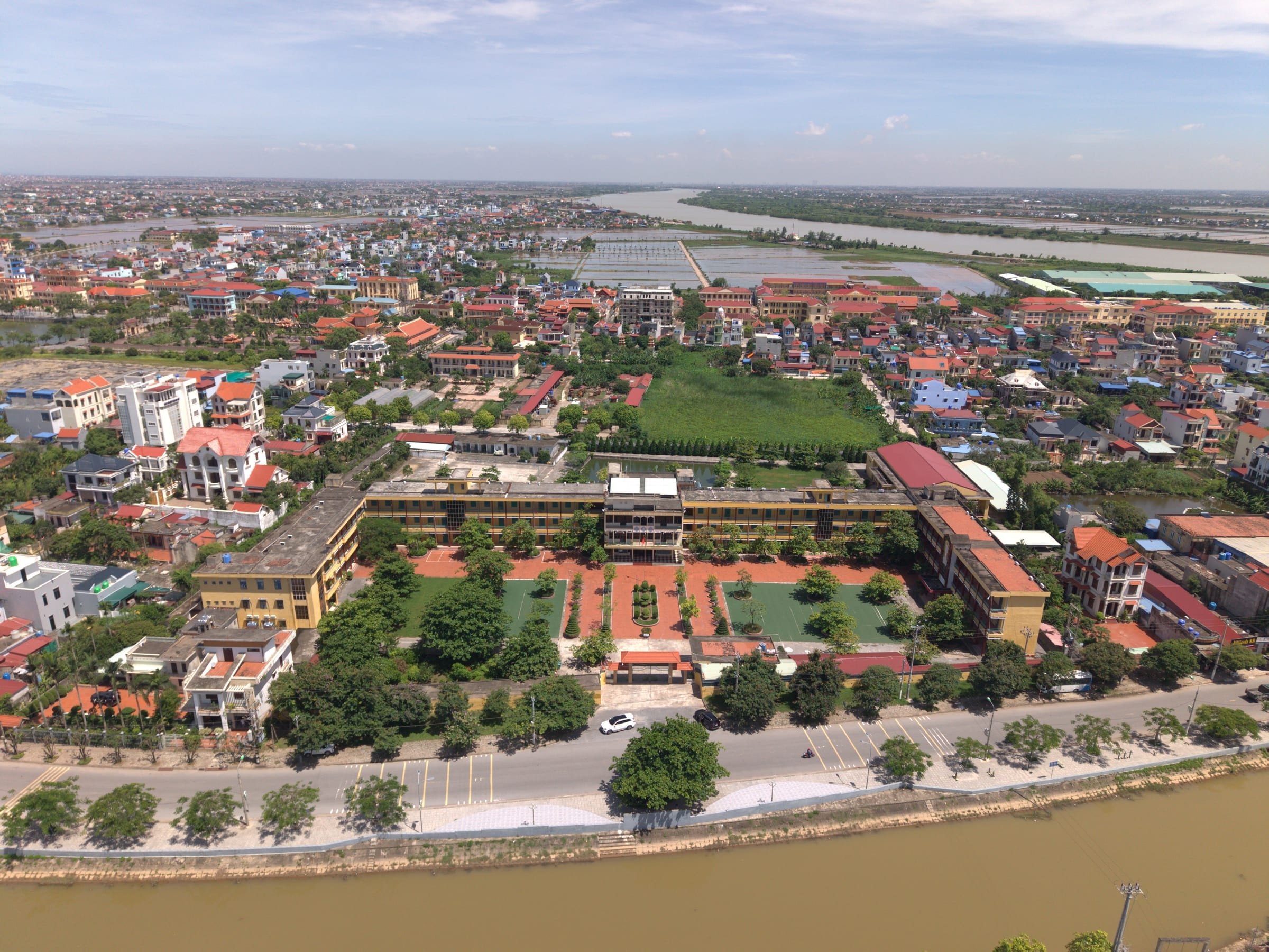 Ảnh flycam trường THPT gần dự án: dãy lớp học quanh sân trường và sân cỏ, phía trước là đường ven sông